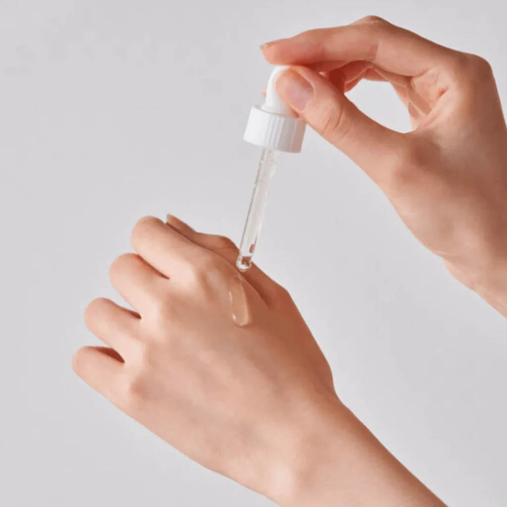 Main tenant une pipette et déposant le sérum sur le dos de sa main.