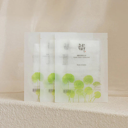 Lot de trois masques en tissu Centella Asiatica Calming Mask de Beauty of Joseon. Sachets blancs translucides illustrés de feuilles de Centella vertes, présentés sur une surface texturée beige minérale.