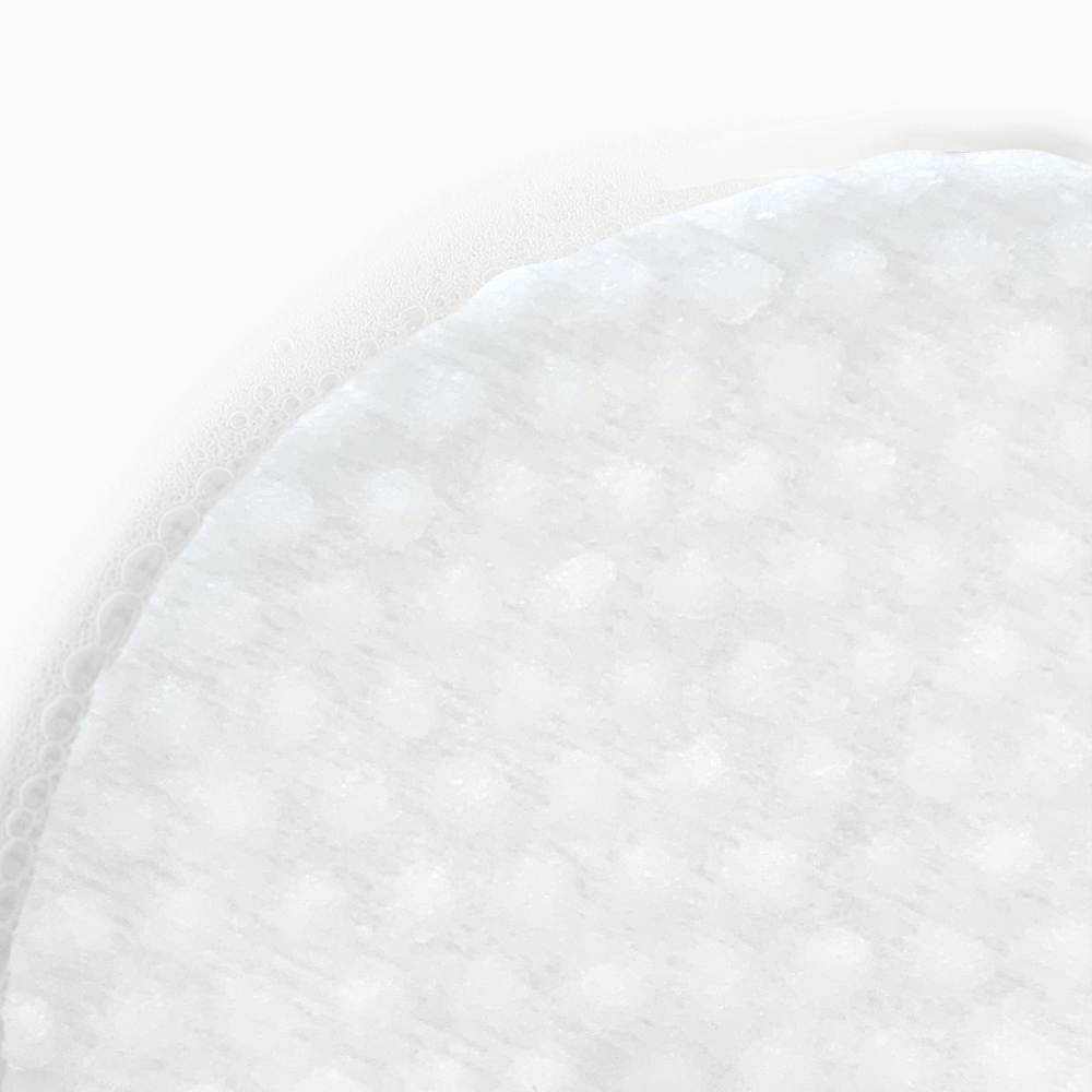 Gros plan sur la texture alvéolée d'un disque de coton ZISU'C. Le pad est saturé de sérum Galacthione pour une exfoliation douce et une hydratation intense de la peau.
