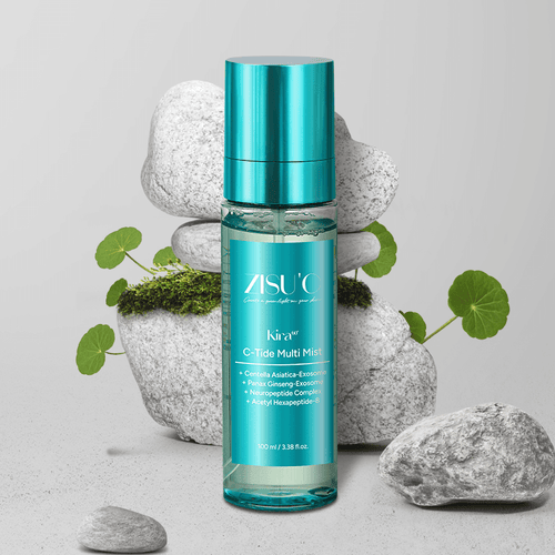 Brume Kira C-Tide Multi Mist de ZISU’C. Flacon transparent avec une étiquette bleu et capuchon bleu sur fond gris avec des galets et des plantes de cica.