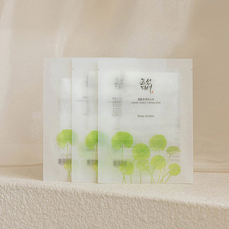Lot de trois masques en tissu Centella Asiatica Calming Mask de Beauty of Joseon. Sachets blancs translucides illustrés de feuilles de Centella vertes, présentés sur une surface texturée beige minérale.