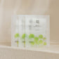 Lot de trois masques en tissu Centella Asiatica Calming Mask de Beauty of Joseon. Sachets blancs translucides illustrés de feuilles de Centella vertes, présentés sur une surface texturée beige minérale.