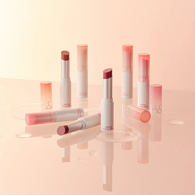 Photo des Glasting Melting Balm De la marque Rom&nd certains sont ouverts laissant voir le contenu du baume d’autres sont fermés le tout sur un fond crème.