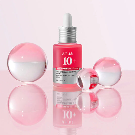 Sérum Niacinamide 10% + TXA 4% de chez ANUA dans un flacon en verre transparent laissant voir la couleur rose du sérum, applicateur pipette, sur fond rose entouré de bulles roses.