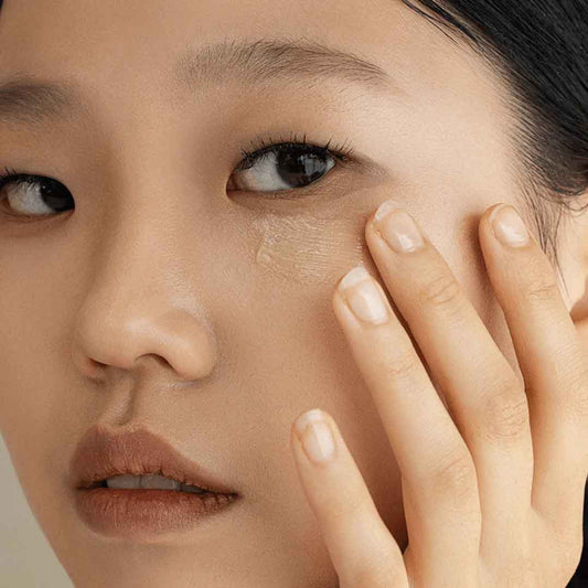 Gros plan sur une personne appliquant une goutte du sérum Revice Serum directement sur sa cerne avec ses doigts.