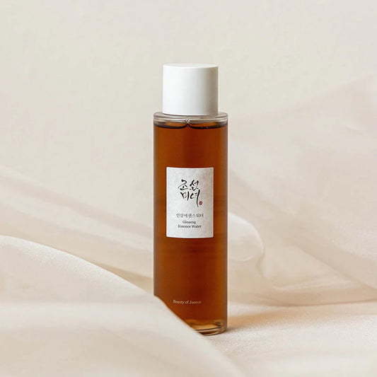 Flacon en plastique transparent du tonique BEAUTY OF JOSEON Ginseng Essence Water de couleur orange sur un voile de tissu crème.