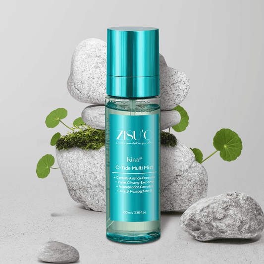 Brume Kira C-Tide Multi Mist de ZISU’C. Flacon transparent avec une étiquette bleu et capuchon bleu sur fond gris avec des galets et des plantes de cica.
